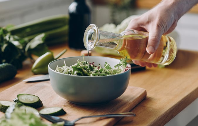 En person som häller olja på en sallad.