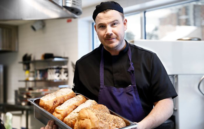 Kock i storkök som håller ett bleck med nybakat bröd