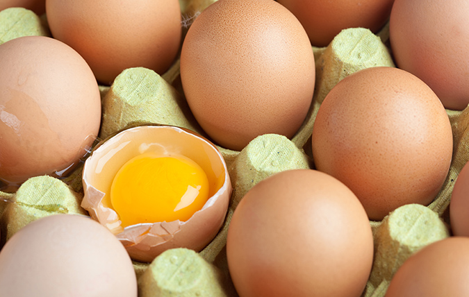 Förpackning med ägg - ett av äggen är knäckt och man ser den råa gulan